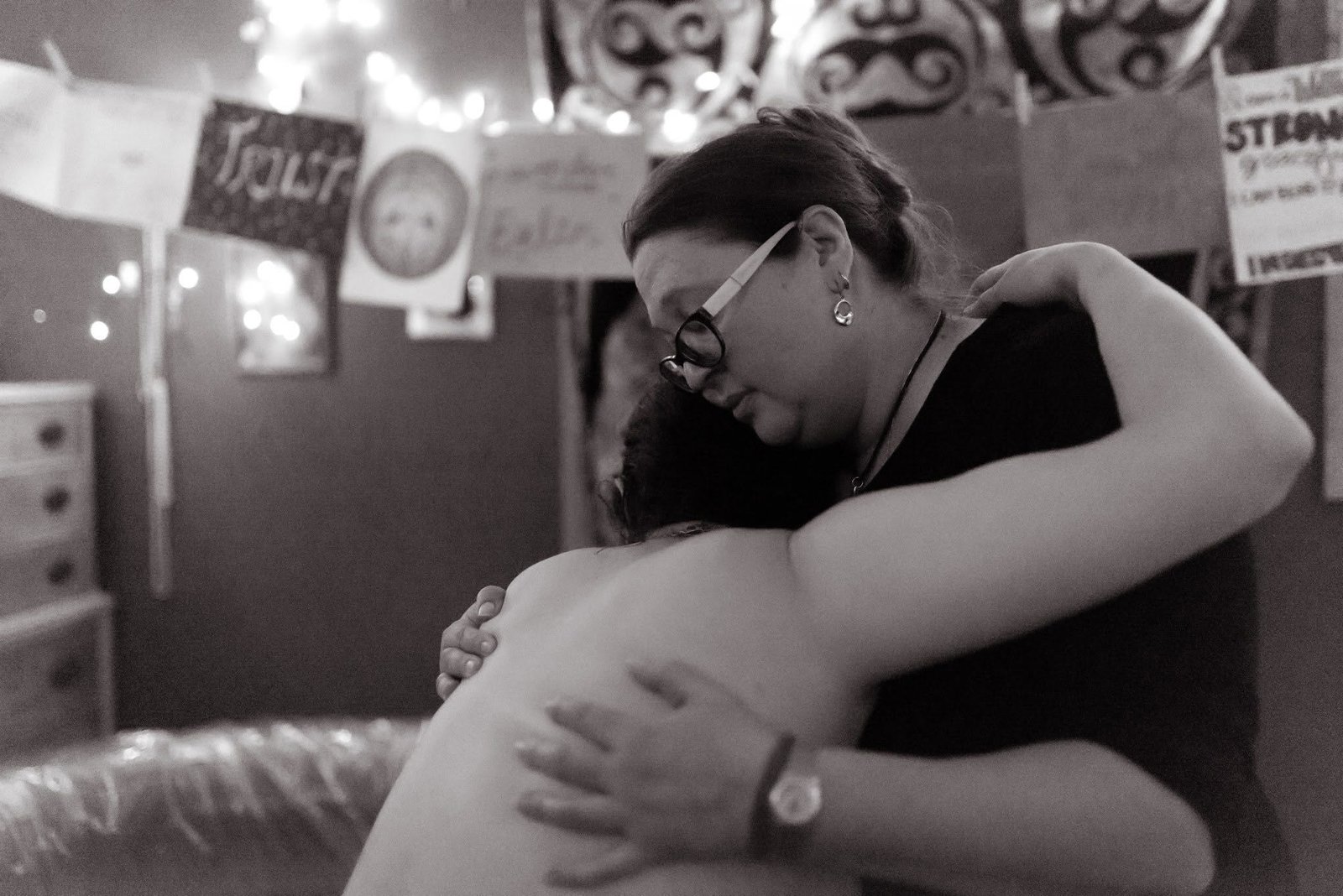Midwife Juliet Dietsch holding a labouring client close, forehead to forehead, in a home birth space hung with string lights and birth affirmation cards